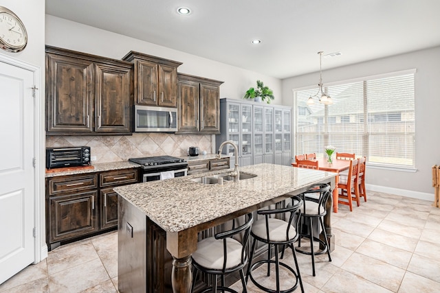 kitchen with a kitchen island with sink, sink, stainless steel appliances, and dark brown cabinetry