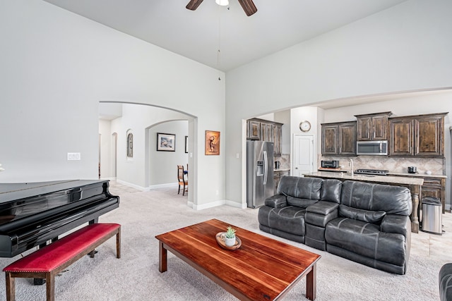 carpeted living room with ceiling fan and a high ceiling