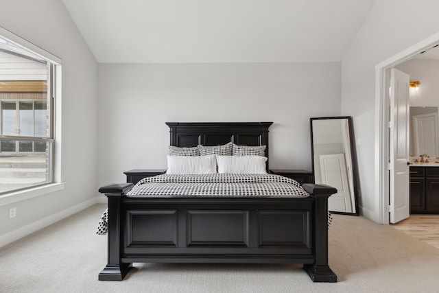 bedroom featuring lofted ceiling, sink, light carpet, and ensuite bath