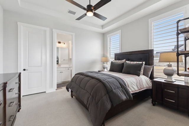 bedroom with light carpet, ensuite bath, a raised ceiling, and visible vents