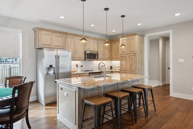 kitchen featuring light brown cabinetry, appliances with stainless steel finishes, a sink, light stone countertops, and hardwood / wood-style flooring