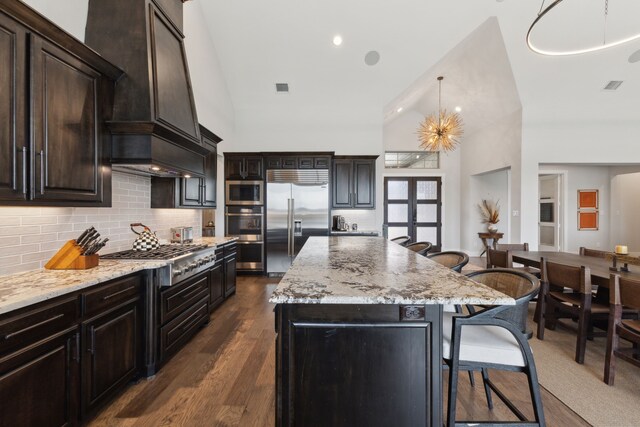 kitchen featuring dark wood-type flooring, a kitchen breakfast bar, a center island, built in appliances, and light stone counters