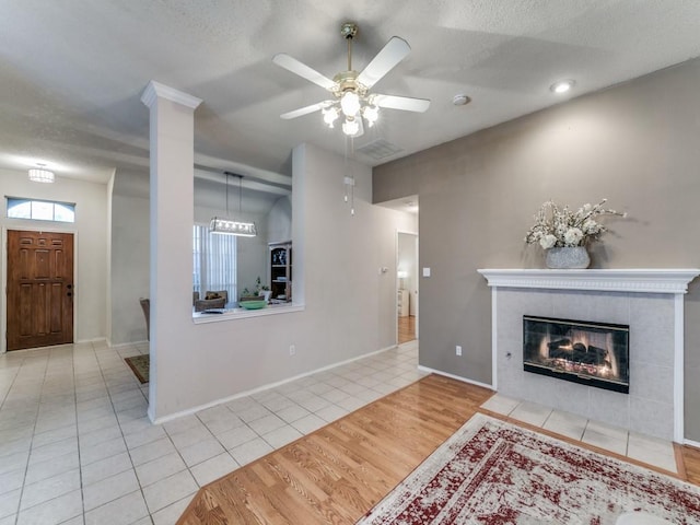 living room with ceiling fan, a textured ceiling, a fireplace, and light hardwood / wood-style floors