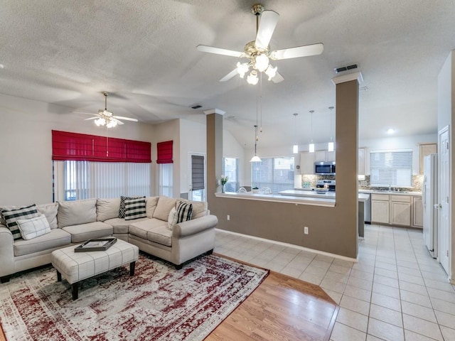 living room with lofted ceiling, light tile patterned floors, sink, ceiling fan, and a textured ceiling