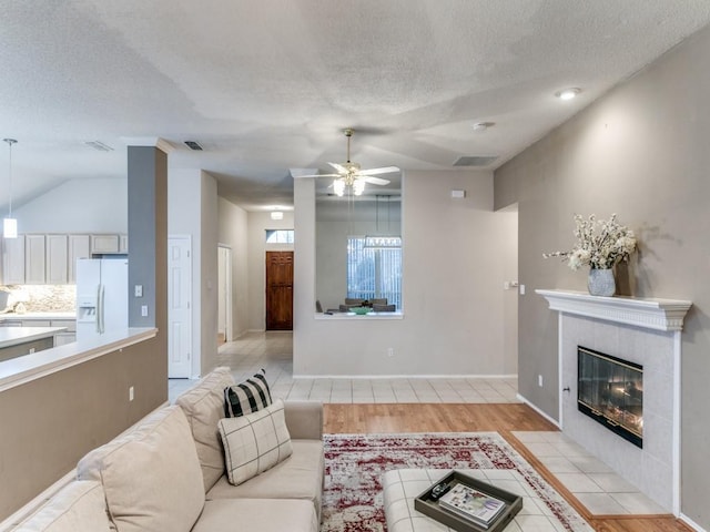 living room featuring lofted ceiling, a textured ceiling, ceiling fan, a fireplace, and light hardwood / wood-style floors