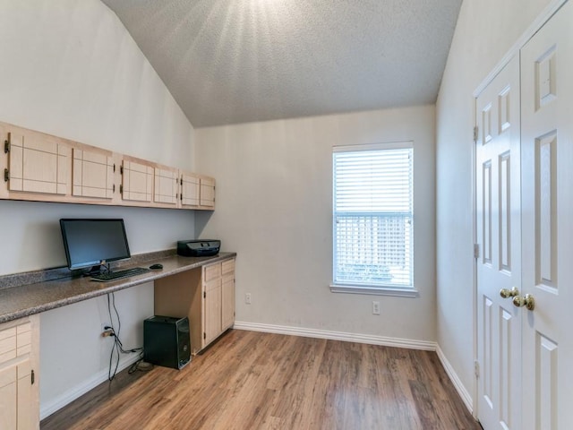 office space featuring built in desk, vaulted ceiling, a textured ceiling, and light wood-type flooring