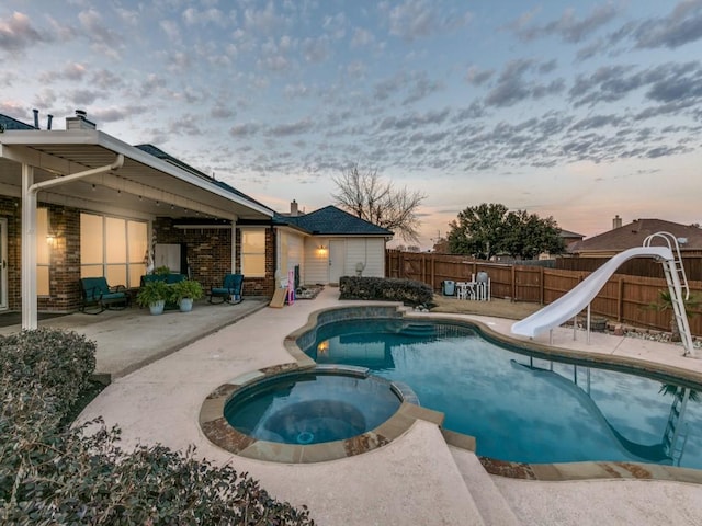 pool at dusk featuring an in ground hot tub, a water slide, and a patio area