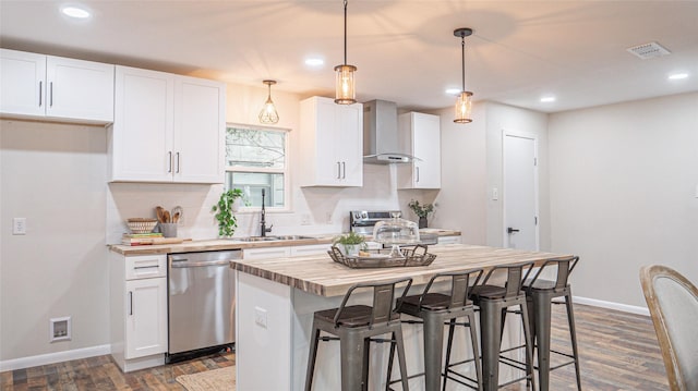 kitchen featuring hanging light fixtures, appliances with stainless steel finishes, white cabinets, and wall chimney exhaust hood