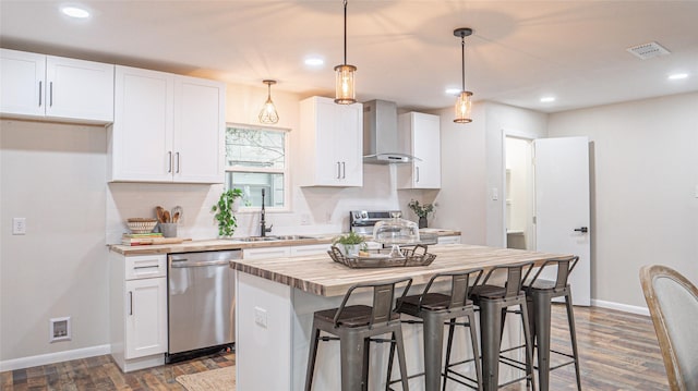 kitchen featuring sink, white cabinets, hanging light fixtures, stainless steel appliances, and wall chimney exhaust hood