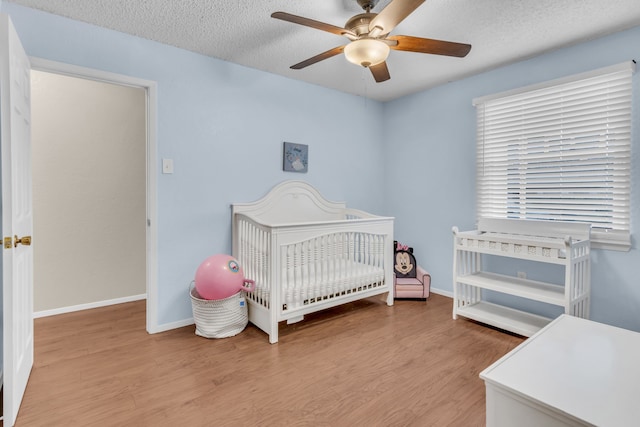 bedroom featuring a crib, ceiling fan, a textured ceiling, and light hardwood / wood-style flooring