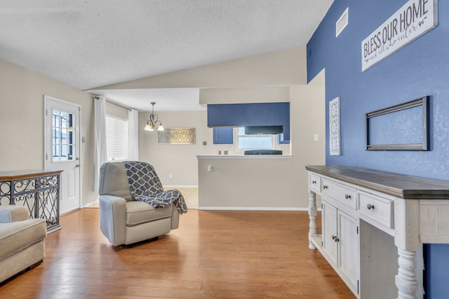 living room featuring lofted ceiling, a chandelier, a textured ceiling, and light wood-type flooring