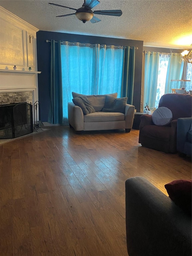 living room featuring wood-type flooring, ceiling fan with notable chandelier, a fireplace, and a textured ceiling