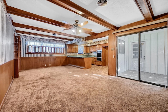 kitchen featuring wood walls, light carpet, kitchen peninsula, double oven, and beam ceiling