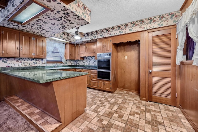 kitchen with double oven, dark stone counters, ceiling fan, kitchen peninsula, and a textured ceiling