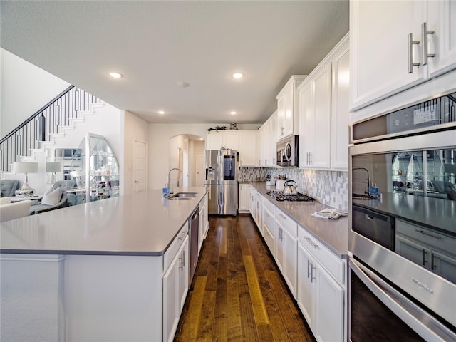 kitchen featuring appliances with stainless steel finishes, sink, white cabinets, backsplash, and a large island with sink