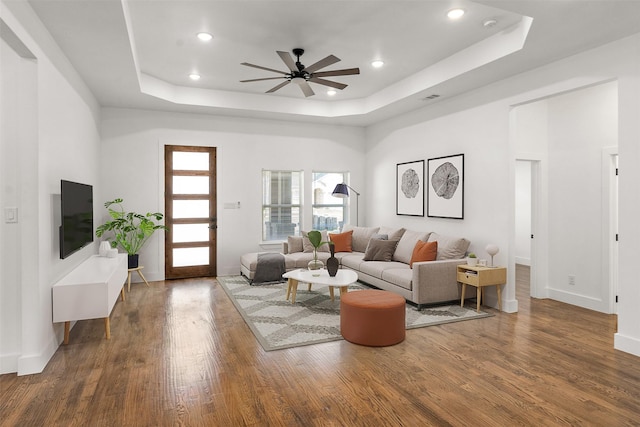 living room with a tray ceiling, dark wood-type flooring, and ceiling fan