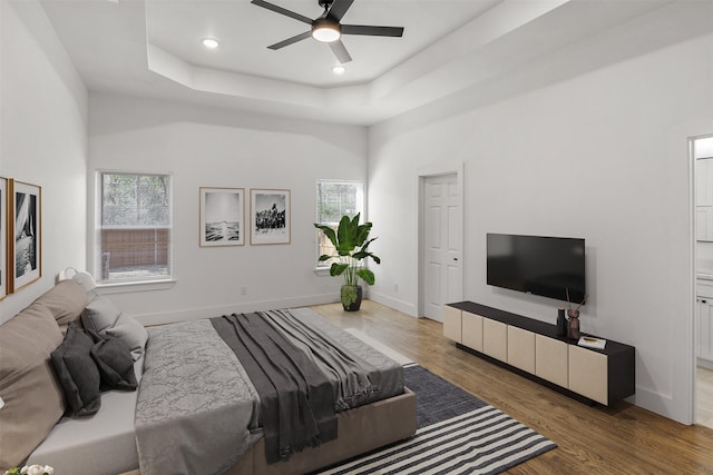 bedroom with hardwood / wood-style flooring, ceiling fan, a raised ceiling, and a towering ceiling