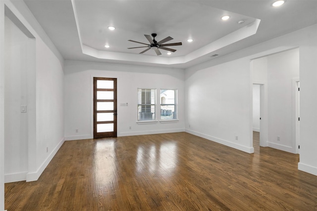 unfurnished living room with a raised ceiling, dark hardwood / wood-style floors, and ceiling fan