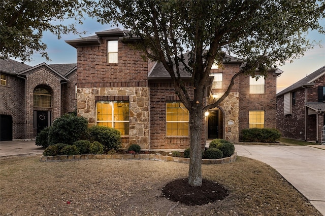 view of front facade featuring stone siding, a shingled roof, a front yard, and brick siding