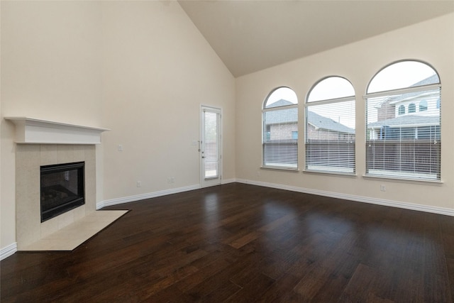 unfurnished living room with high vaulted ceiling, dark wood-style flooring, a tile fireplace, and baseboards