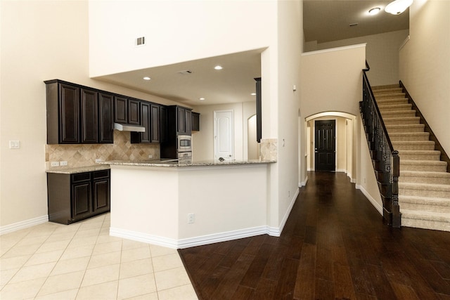 kitchen featuring arched walkways, dark brown cabinetry, baseboards, backsplash, and light stone countertops