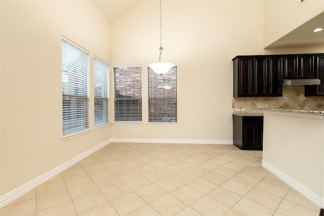 kitchen featuring pendant lighting, light tile patterned floors, backsplash, under cabinet range hood, and baseboards