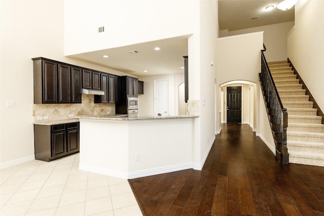 kitchen featuring a high ceiling, light stone countertops, decorative backsplash, light wood-style floors, and arched walkways
