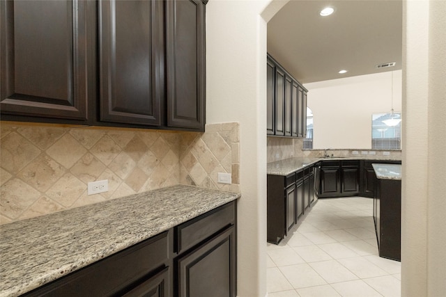 kitchen featuring arched walkways, visible vents, a sink, dark brown cabinets, and light stone countertops