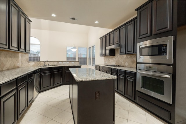 kitchen featuring light tile patterned floors, a kitchen island, a sink, hanging light fixtures, and appliances with stainless steel finishes