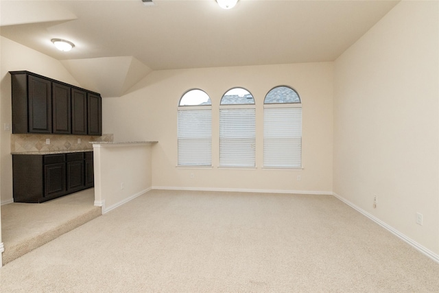 unfurnished living room with lofted ceiling, baseboards, and light colored carpet