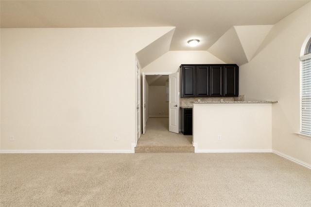 interior space featuring light carpet, baseboards, backsplash, and lofted ceiling