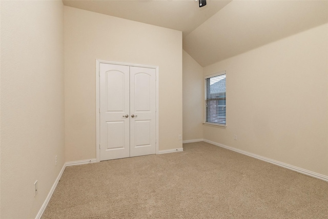 unfurnished bedroom with lofted ceiling, a closet, carpet, and baseboards