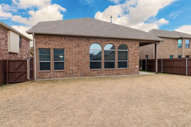 back of house featuring a patio area, a fenced backyard, roof with shingles, and brick siding