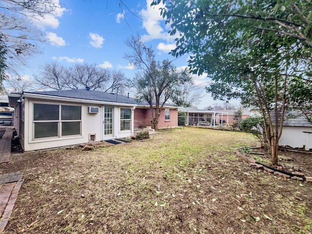 rear view of property with an AC wall unit, a sunroom, and a lawn