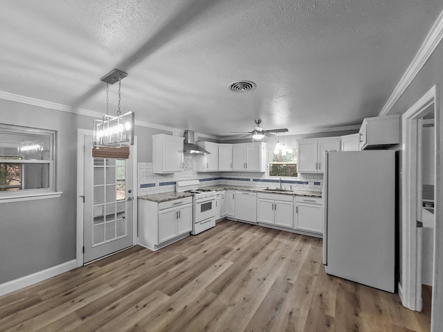 kitchen with pendant lighting, white appliances, ornamental molding, white cabinets, and wall chimney exhaust hood