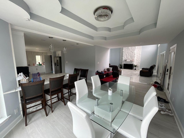 dining room with a stone fireplace and a tray ceiling