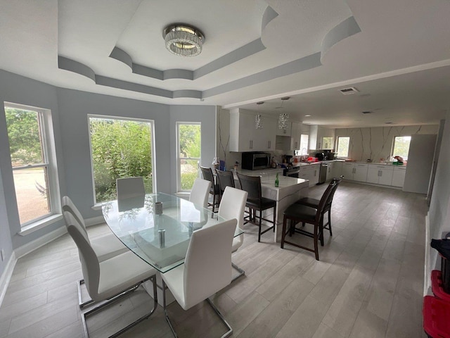 dining area featuring plenty of natural light, light hardwood / wood-style floors, and a raised ceiling