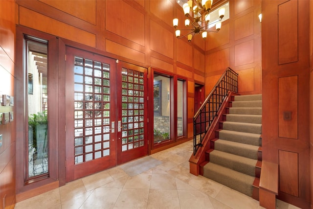 tiled entrance foyer with a towering ceiling, an inviting chandelier, wooden walls, and french doors