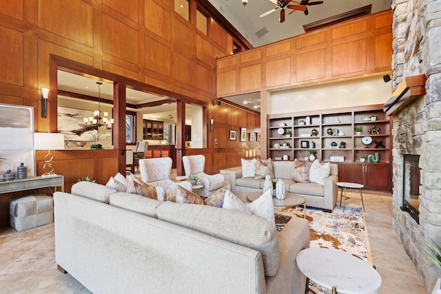 living room featuring a towering ceiling, a fireplace, ceiling fan with notable chandelier, and wood walls