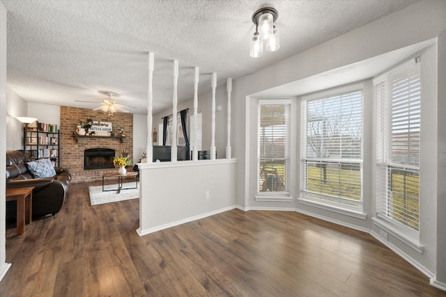 living room featuring ceiling fan, a fireplace, dark hardwood / wood-style floors, and a textured ceiling