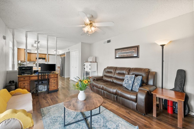 living room featuring dark wood-type flooring, ceiling fan, and a textured ceiling