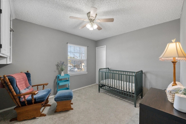 carpeted bedroom with ceiling fan, a nursery area, and a textured ceiling