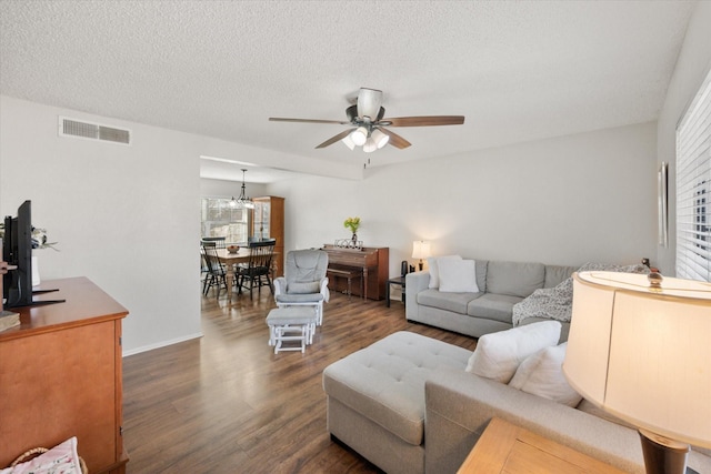 living room featuring dark hardwood / wood-style flooring, ceiling fan with notable chandelier, and a textured ceiling