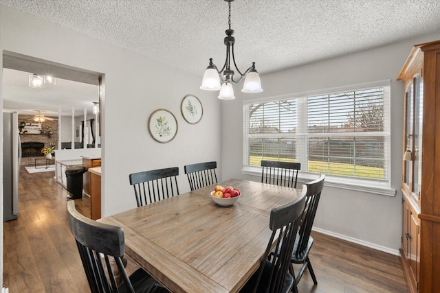 dining space featuring dark hardwood / wood-style floors, a textured ceiling, a brick fireplace, and a notable chandelier