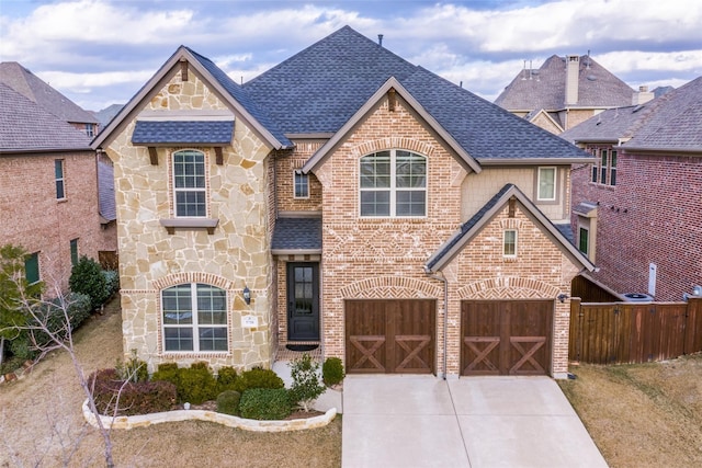 view of front of property featuring a shingled roof, concrete driveway, stone siding, fence, and brick siding