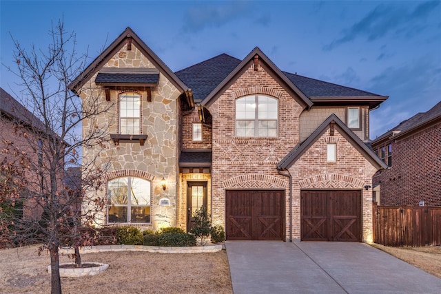 french country style house featuring stone siding, brick siding, roof with shingles, and concrete driveway