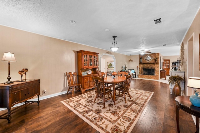 dining space with ceiling fan, a fireplace, dark hardwood / wood-style flooring, and a textured ceiling