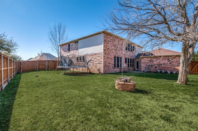 rear view of property with brick siding, a fenced backyard, a trampoline, and a lawn