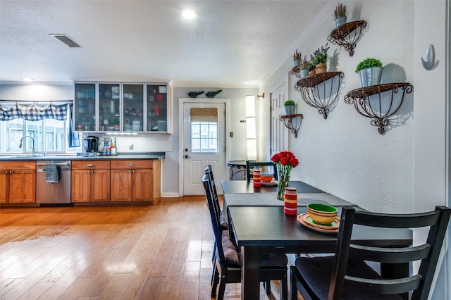 kitchen featuring sink, crown molding, a textured ceiling, light wood-type flooring, and stainless steel dishwasher