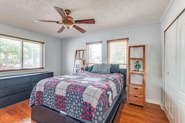 bedroom with a textured ceiling, wood finished floors, a closet, and multiple windows